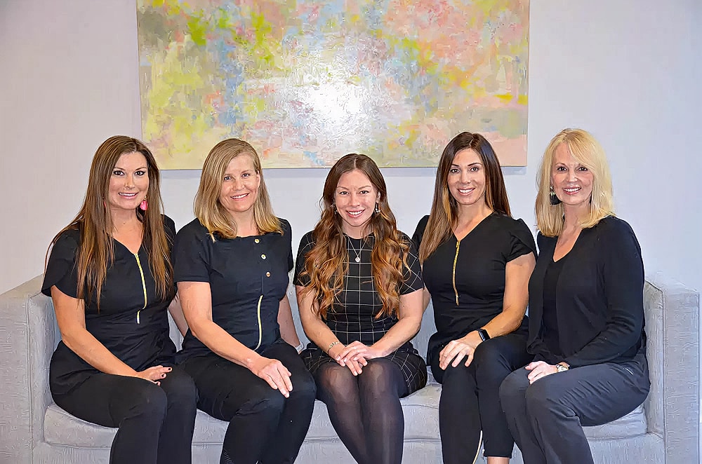 Five women in professional attire smiling together.