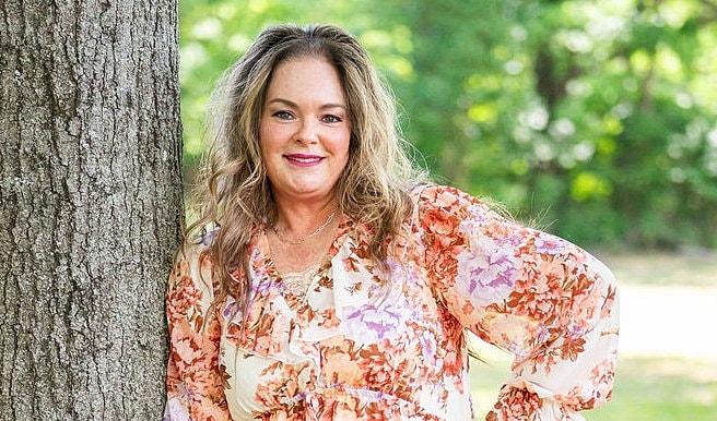 Woman in floral dress leaning against tree.