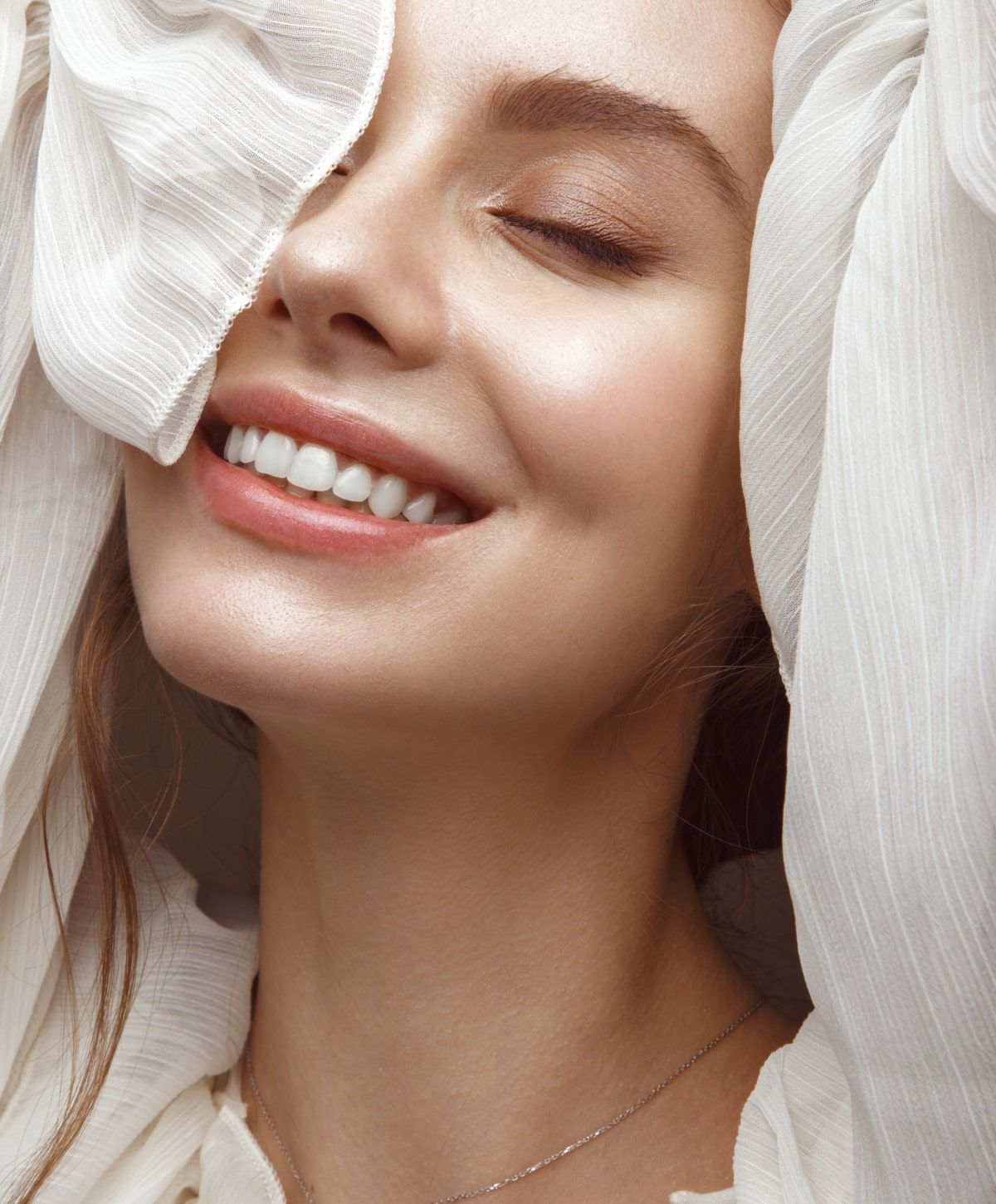Smiling woman with soft, flowing fabric covering face.
