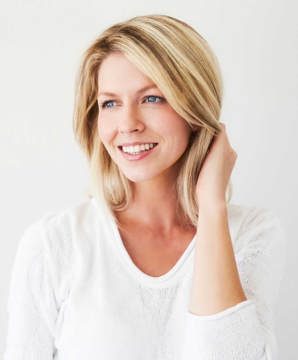 Smiling woman in a white sweater, looking thoughtfully.